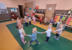 Dzieci trzymają się za ręce w kole na sali gimnastycznej.