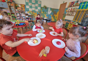 Czworo dzieci wbija wykałaczki w połowę jabłka tworząc jeża.