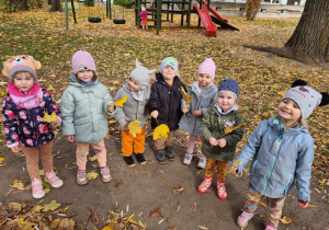 Dzieci pozują do zdjęcia w ogrodzie przedszkolnym trzymając w rękach liście.