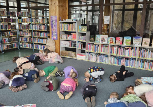 Biblioteka - dzieci leżą skulone na dywanie są bombkami