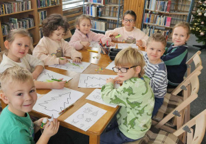 Biblioteka - dzieci siedzą przy stolikach i kolorują choinki