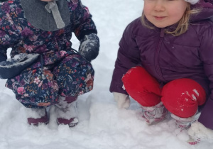 Dwie dziewczynki kucają w ogrodzie przedszkolnym.