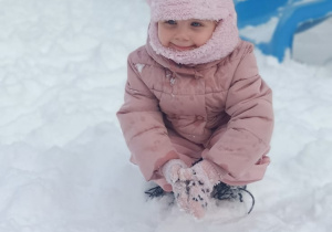 Dziewczynka kuca w ogrodzie przedszkolnym.