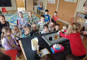 Dzieci zgromadzone wokół stołu na którym soją szklane słoiki