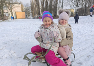 Dwie uśmiechnięte dziewczynki siedzące na sankach