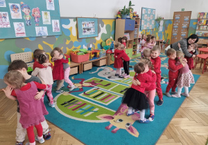 Dzieci na dywanie tańczą i się przytulają podczas zabawy.
