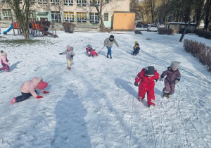 Dzieci podchodzą pod górkę i bawią się na śniegu w ogrodzie przedszkolnym.