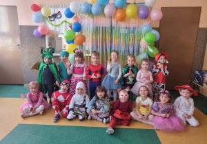 Dzieci pozują do zdjęcia w przebraniach na tle dekoracji karnawałowej.
