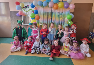 Dzieci pozują do zdjęcia w przebraniach na tle dekoracji karnawałowej.