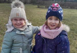 Dwie dziewczynki pozują do zdjęcia w ogrodzie przedszkolnym.