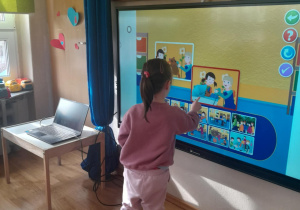 Dziewczynka wykonuje zadania na ekranie multimedialnej.