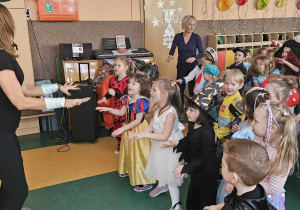 Bal Karnawałowy - dzieci wykonują ruchy do piosenki pokazywanej przez prowadzącą