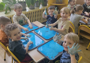 Zabawy cieczą nienewtonowską - dzieci siedzą przy stolikach i bawią się kolorową cieczą