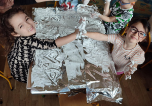 Eksperymenty - dzieci siedzą przy stolikach i malują na folii aluminiowej pianką dogolenia