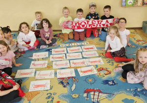 Dzień Kibica - dzieci siedzą na dywanie obok wykonanych przez siebie prac