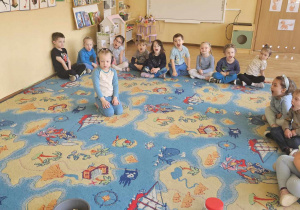 Dzień Świadomości Autyzmu - dzieci siedzą w kole, dziewczynka siedzi w środku koła i ma na głowie słuchawki, reszta dzieci krzyczy