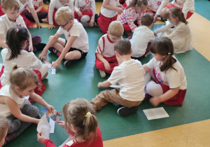Święto Flagi - dzieci siedzą w trzyosobowych zespołach na podłodze i układają obrazek