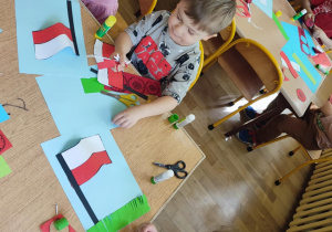 Święto Flagi - dzieci siedzą przy stolikach i przyklejają wycięte flagi na karton