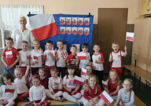 Święto Flagi - dzieci wraz z nauczycielem pozują do zdjęcia na tle dekoracji z wykonanymi przez siebie flagami