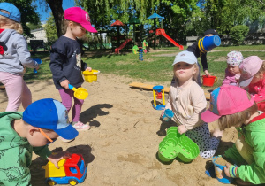 Grupa dzieci bawi się w piaskownicy.