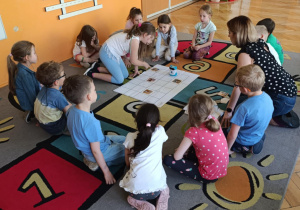 Dzieci siedzą na dywanie i uczestniczą w zajęciach z kodowania