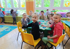 Grupa dzieci siedzi przy stoliku wyklejając kulakmi z bibuły kontury kuli ziemskiej