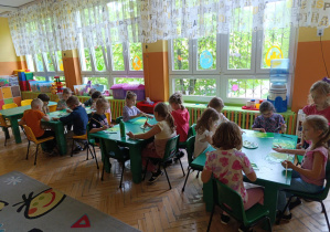 Dzieci siedzą przy stolikach i malują farbami