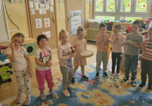 Przedszkolna Orkiestra - dzieci stoją w półkolu i grają na instrumentach