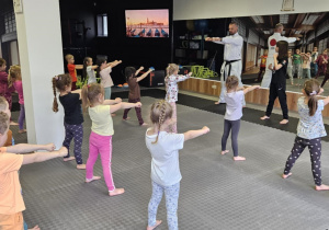 Lekcja sportowa w japońskim DOJO - dzieci stoją na sali i pokazują ruchy prowadzącego