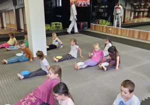 Lekcja sportowa w japońskim DOJO - dzieci z pachołkami na brzuchach poruszają się odpychając rękoma i nogami