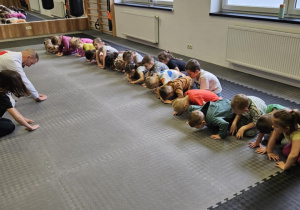Lekcja sportowa w japońskim DOJO - dzieci siedzą na przeciwko prowadzącego i uczą się japońskich ukłonow