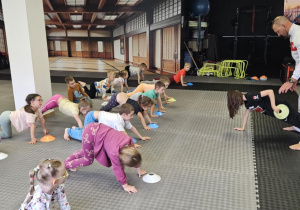 Lekcja sportowa w japońskim DOJO - dzieci podparte na rękach i nogach przekładają pachołek