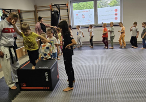 Lekcja sportowa w japońskim DOJO - dzieci ustawione jedno za drugim przechodzą przechodzą przez skrzynie