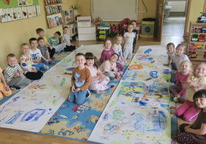 Zajęcia o zwierzętach - dzieci siedzą przy dużych arkuszach papieru i pastelami rysują poznane na zajęciach zwierzęta