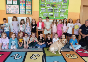 Dzieci pozują do zdjęcia ze strażnikiem miejskim i psem