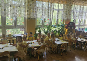 Żółty Dzień - dzieci siedzą przy stolikach i malują żółtą farbą na dużych arkuszach papieru