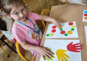 Gimnastyka mózgu - dziewczynka jedną ręką pokazuje kropkę na kartonie druga trzyma na łapce na kartonie