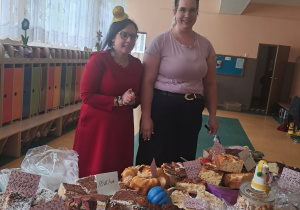 Dwie uśmiechnięte kobiety stoją przy stole z ciastami