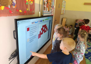 Dzieci odkodowują zakodowany obrazek muchomora na ekranie multimedialnym