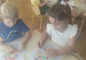 Dziewczynka i chłopiec wyklejają liść kropkami z plasteliny