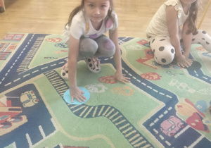 Dziewczynka siedzi na dywanie i zakrywa dłonią dużą kropkę z papieru