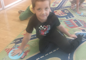 Chłopiec siedzi na dywanie i zakrywa dłonią kropkę z paieru