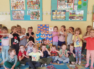 Dzieci pozują przy tablicy z pracami plastycznymi.