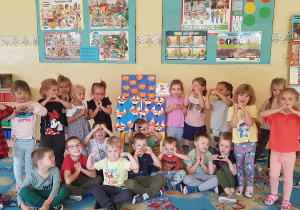 Dzieci pozują przy tablicy z pracami plastycznymi.