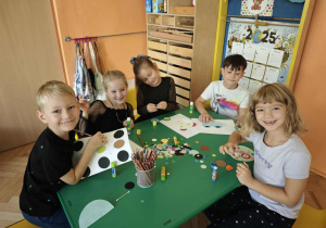 Dzieci siedzące przy stole przyklejają kropki na kartkach