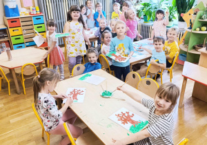 Dzieci siedzą przy stolikach malując farbami