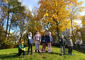 Dzieci stoją na górce i podrzucają jesienne liście