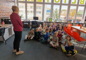 Dzieci siedzą na dywanie i słuchają pani bibliotekarki