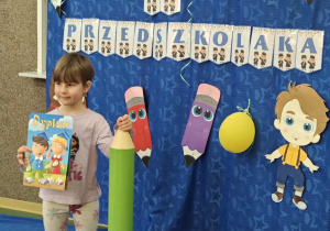 Dziewczynka stojąca z dyplomem i duża kredką