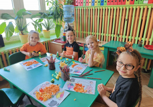 Cztery dziewczynki wyklejają dynię pomarańczową bibułą